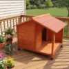 Cabin style wooden outdoor dog house with slant asphalt roof and raised feet on a garden patio deck surrounded by flowers.