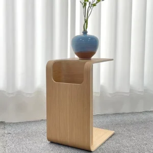 Manna natural bentwood side table flipped vertically as a high C-shaped sofa table with a ceramic vase against white curtains.