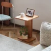 Manna cherry wood C-shaped side table styled in a living room corner with a small potted plant on the base shelf and a photo frame on top.