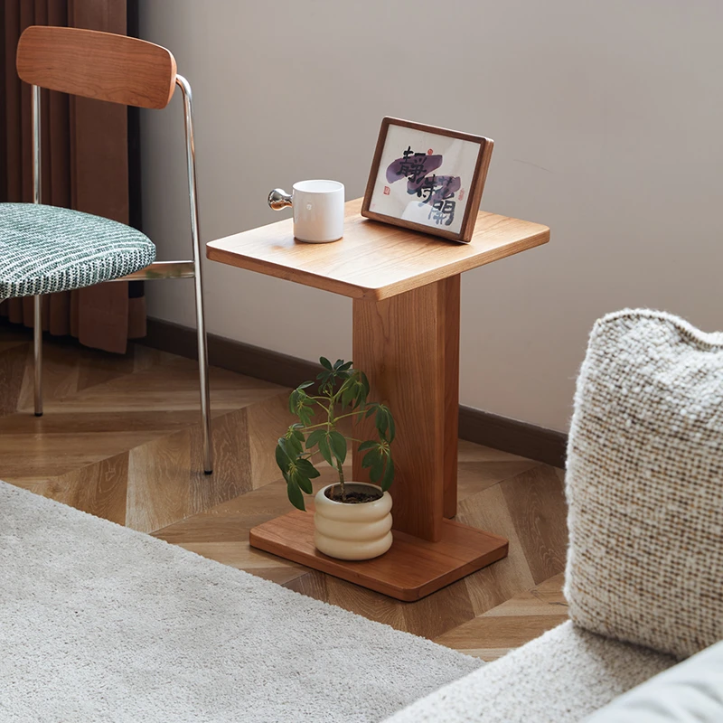 Manna cherry wood C-shaped side table styled in a living room corner with a small potted plant on the base shelf and a photo frame on top.