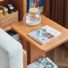 Close-up view of Manna cherry wood C-shaped side table next to a sofa with a glass kettle and a book.