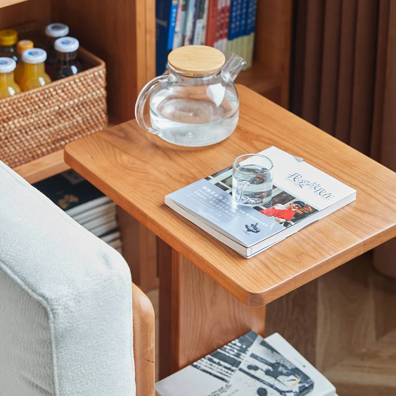 Close-up view of Manna cherry wood C-shaped side table next to a sofa with a glass kettle and a book.
