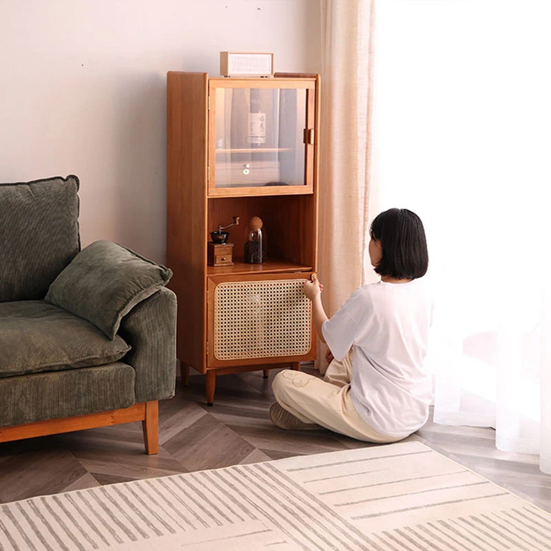 Manna cherry wood side cabinet with glass display and rattan door styled in a living room with a person sitting on the floor.