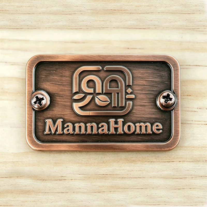 Close-up view of MannaHome antique bronze metal logo badge plate with screws mounted on solid wood furniture.
