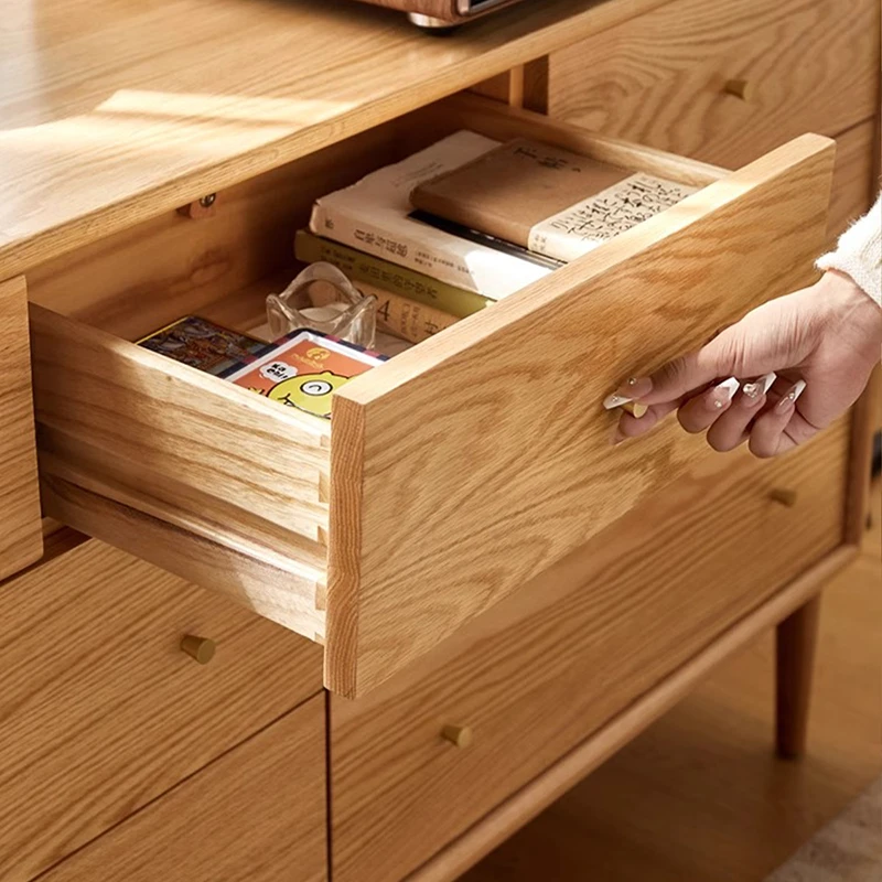 Close-up view of a hand pulling open a smooth solid wood drawer with a brass knob on Manna oak 7-drawer dresser.
