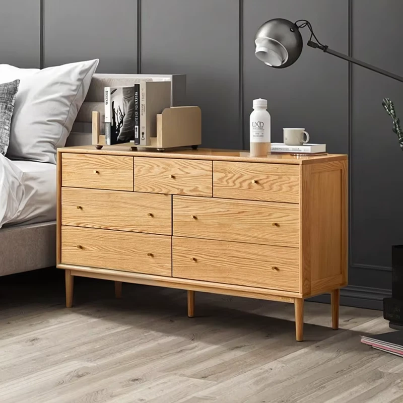 Front view of Manna oak 7-drawer wide chest of drawers styled against a modern dark gray feature wall in a bedroom.