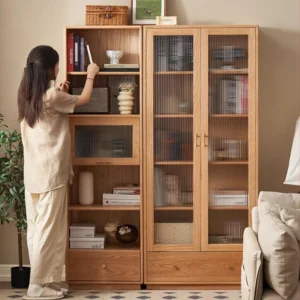 A person selecting books from Manna oak single door and double door fluted glass bookcases placed side-by-side in a living room.