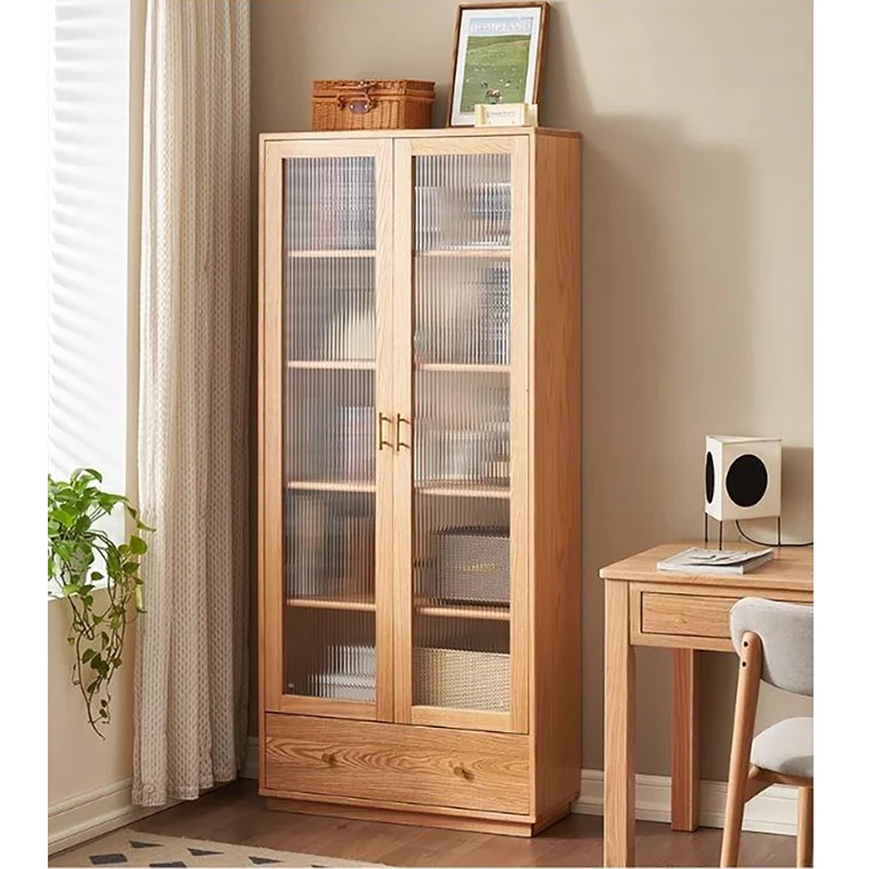 Manna oak double door bookcase with fluted glass doors and bottom drawer styled next to a wooden desk in a room.