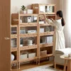 manna-oak-glass-door-bookcase-3-heights-living-room. Manna oak bookcases with retractable glass flip doors in three height options 1.2m, 1.5m, and 1.8m styled with a woman in a living room.