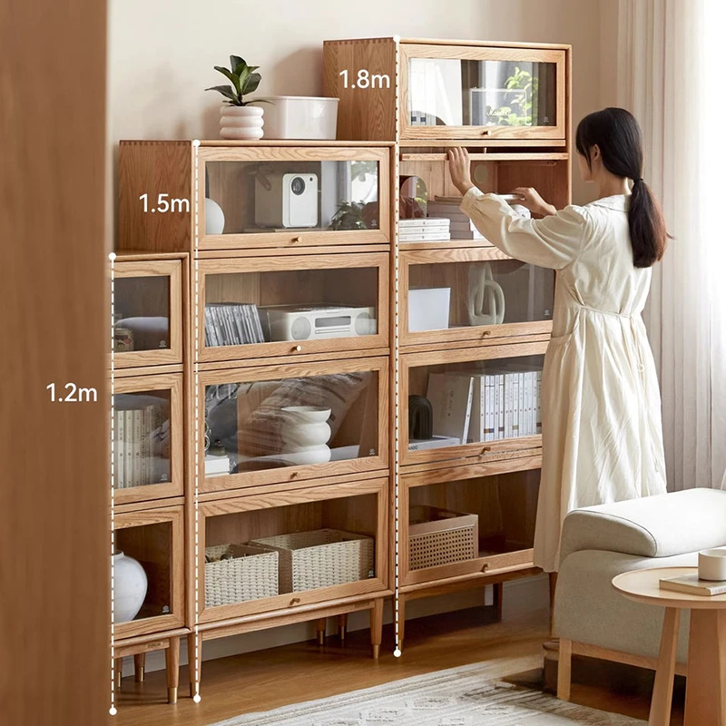 manna-oak-glass-door-bookcase-3-heights-living-room. Manna oak bookcases with retractable glass flip doors in three height options 1.2m, 1.5m, and 1.8m styled with a woman in a living room.