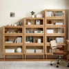 manna-oak-glass-door-bookcases-3-tier-4-tier-5-tier-setup Manna oak glass door bookcases in 3-tier, 4-tier, and 5-tier configurations arranged side-by-side in a modern home office with a desk chair.