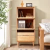 manna-oak-glass-flip-door-bookcase-sofa-sideboard Front view of Manna oak bookcase with flip-up glass door holding magazines like Cereal, placed next to a wooden sofa.