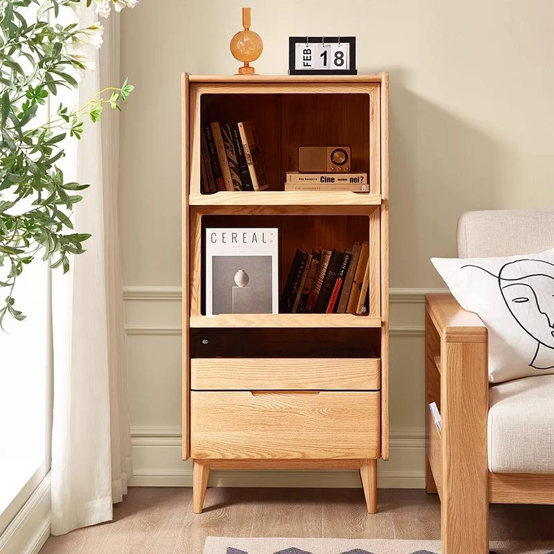 manna-oak-glass-flip-door-bookcase-sofa-sideboard Front view of Manna oak bookcase with flip-up glass door holding magazines like Cereal, placed next to a wooden sofa.
