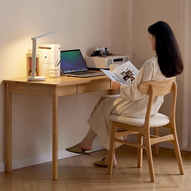 A person sitting on a Manna oak horn-back upholstered chair reading at a solid wood desk in a home office setup.