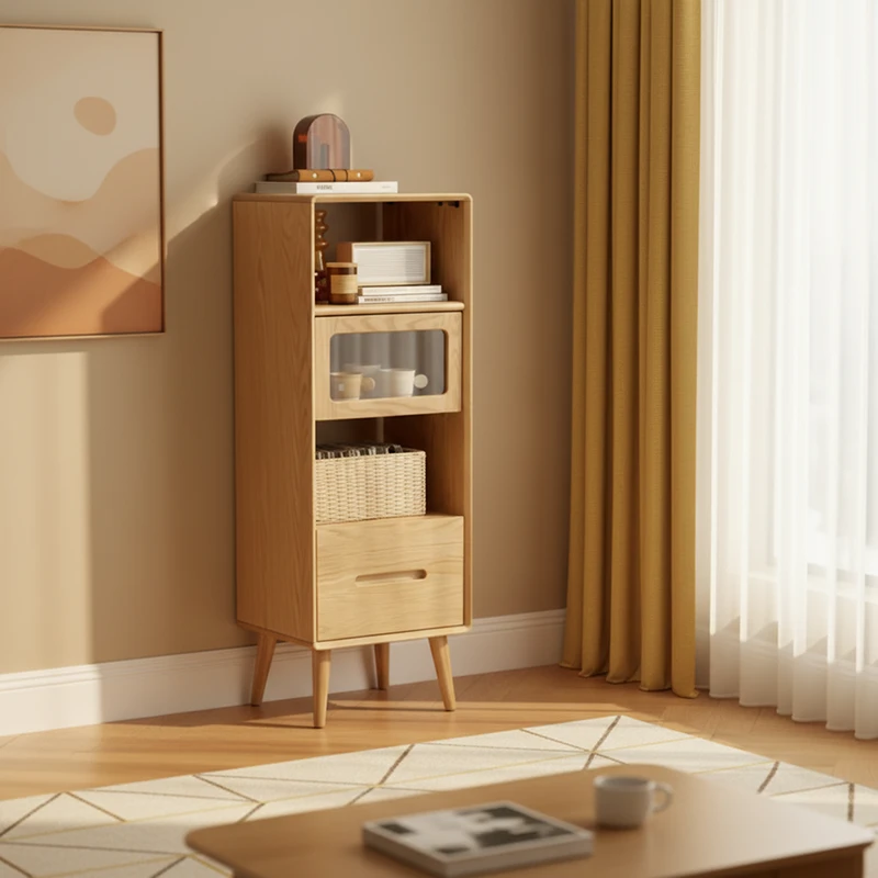Manna oak tall narrow accent cabinet with glass flip door, open shelf, and bottom drawer styled in a warm living room corner.
