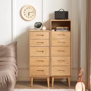 Front view comparison of Manna oak narrow 5-drawer chest and tall chest with open shelf holding books and a Bluetooth speaker.