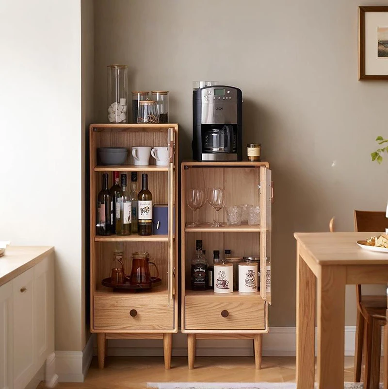 Two Manna oak narrow glass cabinets in 118cm and 100cm heights arranged side-by-side as a coffee bar credenza in a dining area.