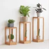 Manna oak open frame side table used as a bedside nightstand holding stacked books, a small ornament, and a coffee cup.