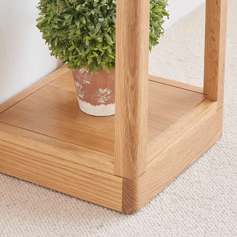 Close-up view of the bottom shelf and solid corner joint of Manna oak open frame plant stand with a potted plant.