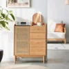 manna-oak-rattan-accent-cabinet-4-drawers-living-room Manna oak accent cabinet with rattan mesh door and 4 drawers styled in a bright living room next to a white sofa.