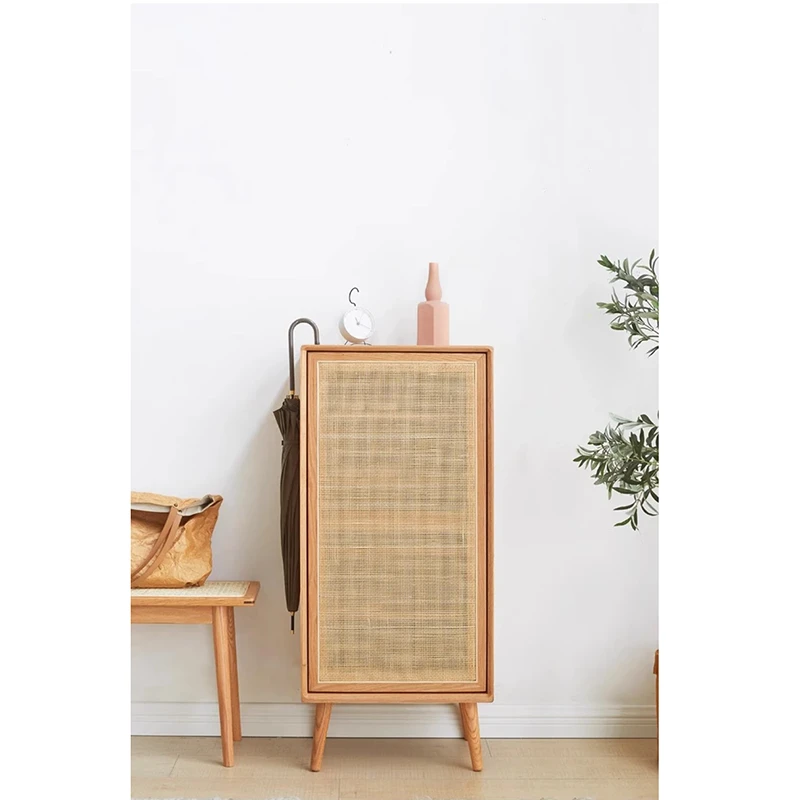 Front view of Manna oak slim shoe cabinet with woven rattan door and tapered wooden legs placed in an entryway.