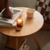 Top view detail of Manna oak round side table showcasing natural wood grain texture, a burning scented candle, and a coffee cup.