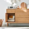 Close-up view of open single door cabinet compartment on Manna oak sideboard credenza holding storage bins and blankets.