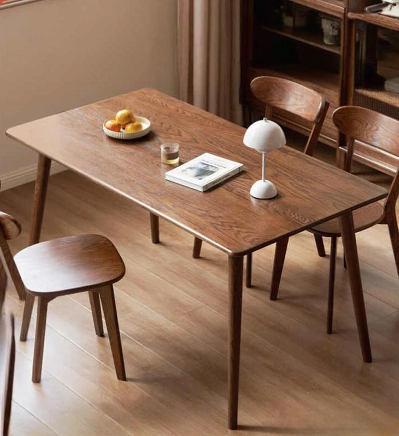 Mid-century modern solid wood dining table with tapered legs and rounded corners in a warm dining room setting.