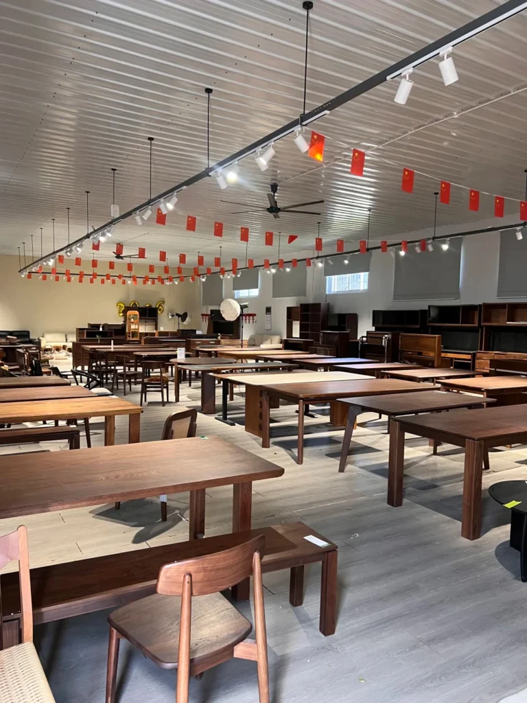 Spacious factory furniture showroom displaying a wide collection of solid wood dining tables, desks, and matching chairs.