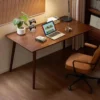 Dark wood study computer desk with laptop, green potted plant, and ergonomic leather chair in a cozy home office.