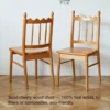manna-cherry-dining-chair-spindle-back-front-view Front view of two solid cherry wood dining chairs with spindle backs and carved crests against a white wall.