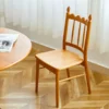 manna-cherry-dining-chair-spindle-back-lifestyle Solid cherry wood dining chair with a scalloped spindle backrest and finials beside a round wooden table.