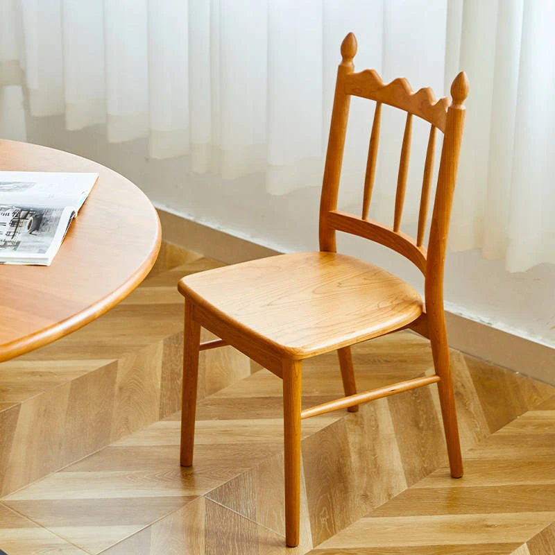 manna-cherry-dining-chair-spindle-back-lifestyle Solid cherry wood dining chair with a scalloped spindle backrest and finials beside a round wooden table.