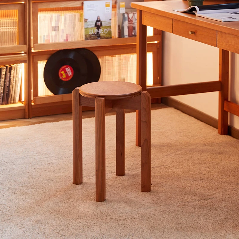 manna-cherry-stackable-stool-living-room Lifestyle view of round cherry wood stackable stool with through tenon legs standing in a living room beside a wooden desk.