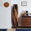 manna-cherry-stackable-stool-stacked Six solid cherry wood round stackable stools nested in a tall space saving stack against a white wall beneath a wooden clock.