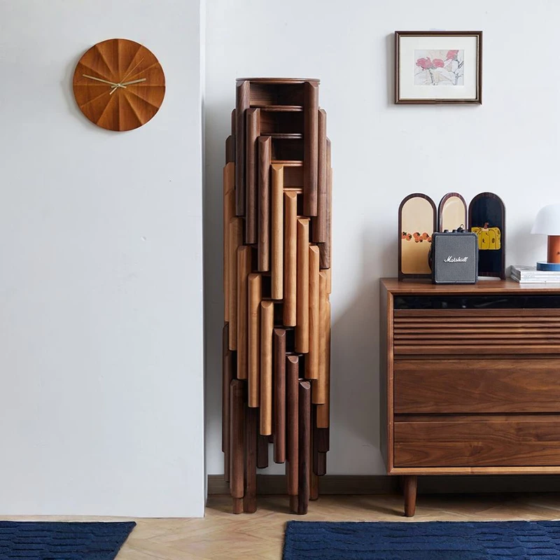 manna-cherry-stackable-stool-stacked Six solid cherry wood round stackable stools nested in a tall space saving stack against a white wall beneath a wooden clock.