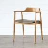 Front view of a solid oak armchair with curved wood armrests and a grey leather upholstered seat on pale flooring.