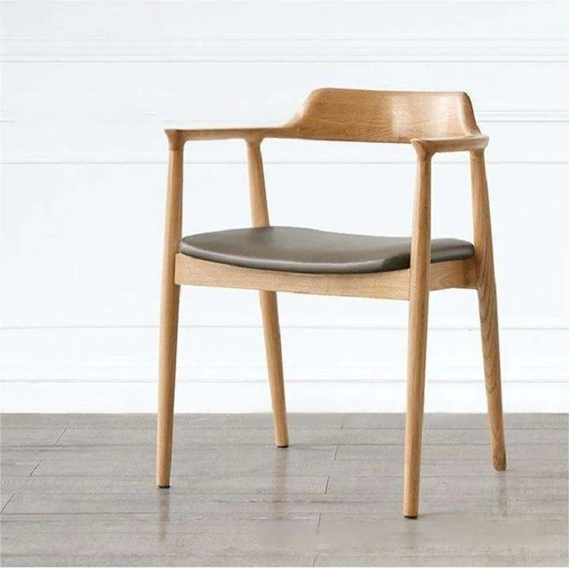 Front view of a solid oak armchair with curved wood armrests and a grey leather upholstered seat on pale flooring.