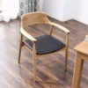 Solid oak armchair with a black leather seat cushion placed on dark wood flooring in a bright interior setting.