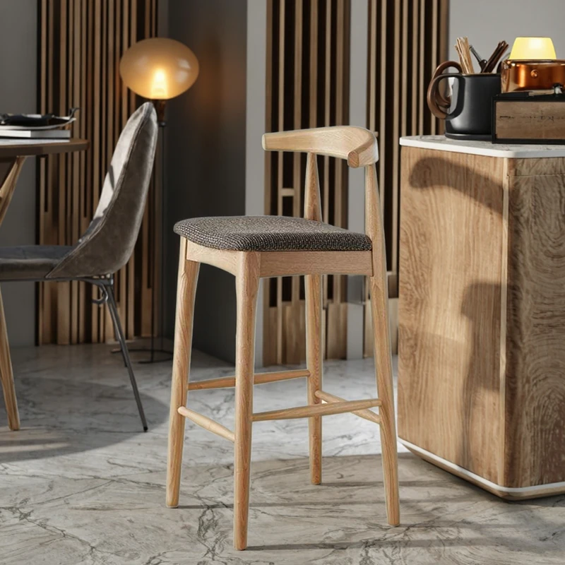 manna-oak-bar-stool-woven-seat-lifestyle Lifestyle view of oak bar stool with curved low backrest and grey woven fabric seat beside a kitchen island with marble top.