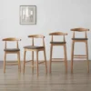 manna-oak-bar-stool-woven-seat-size-guide Four oak bar stools with grey woven upholstered seats in increasing counter, bar and extra tall heights against a white wall.