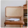 Detail view of the woven cane backrest and tan tufted leather seat of an oak cantilever dining chair with a book on it.