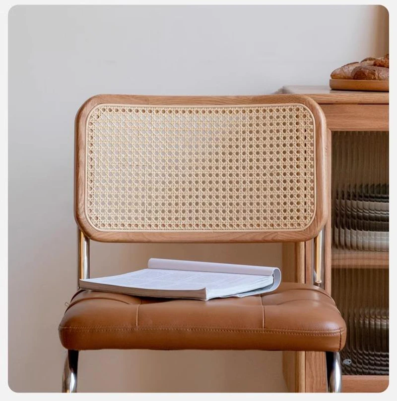 Detail view of the woven cane backrest and tan tufted leather seat of an oak cantilever dining chair with a book on it.