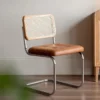Living room view of an oak cane back cantilever dining chair with a tan tufted leather seat beside a wood cabinet.