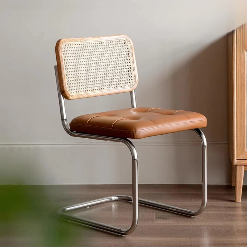 Living room view of an oak cane back cantilever dining chair with a tan tufted leather seat beside a wood cabinet.