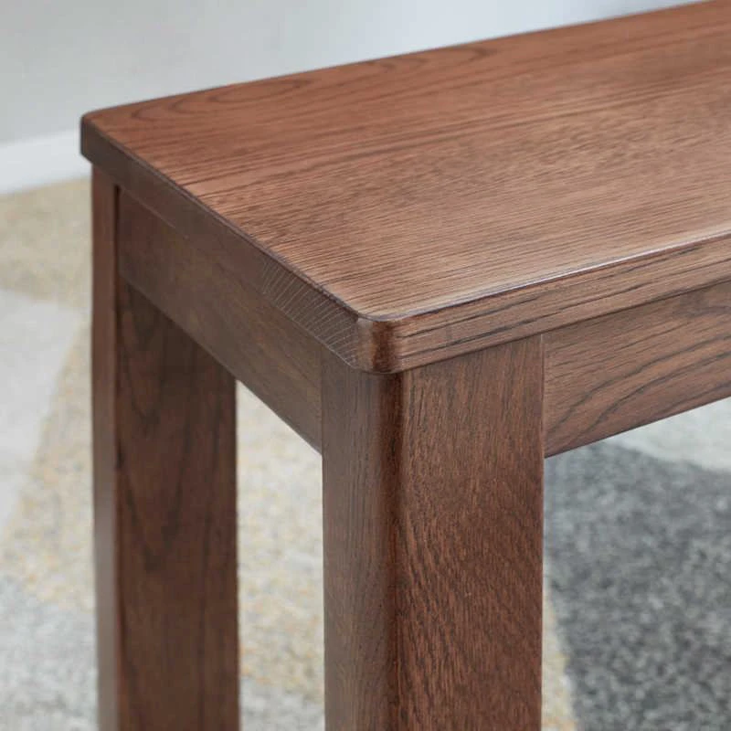 manna-oak-dining-bench-corner-detail Detail view of a dark brown oak bench corner showing the rounded seat edge and square mortise leg joint.