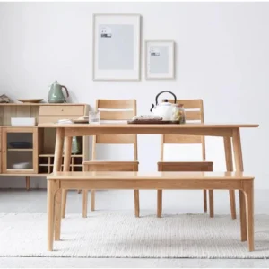 Oak dining bench placed in front of an oak dining table with two spindle chairs in a bright modern dining room.