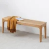 manna-oak-dining-bench-front-view-cd1004 Front view of a solid oak dining bench with curved leg brackets styled with a mustard throw and a closed magazine.