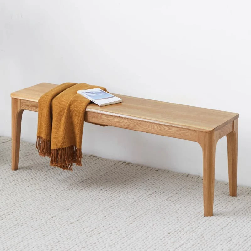 manna-oak-dining-bench-front-view-cd1004 Front view of a solid oak dining bench with curved leg brackets styled with a mustard throw and a closed magazine.