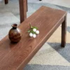manna-oak-dining-bench-material-detail-cd1003 Close-up of the reddish brown oak bench seat showing the oak grain pattern and a small ceramic vase.